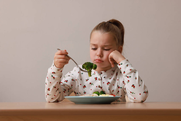 Cute little girl refusing to eat her dinner at table on grey background - Foto, Imagem