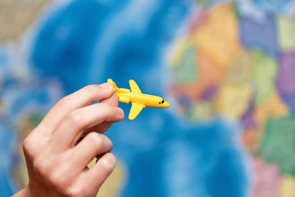 A child's hand holds a toy plane model against the background of a world map - Photo, Image
