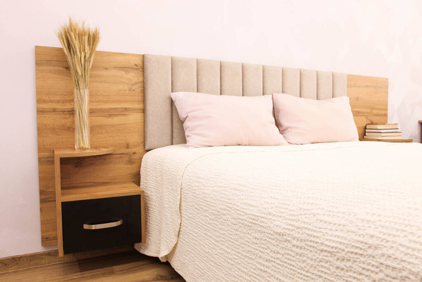 Ξύλινο κρεβάτι με λευκό κάλυμμα κρεβατιού σε φωτεινό χώρο.  - Φωτογραφία, εικόνα