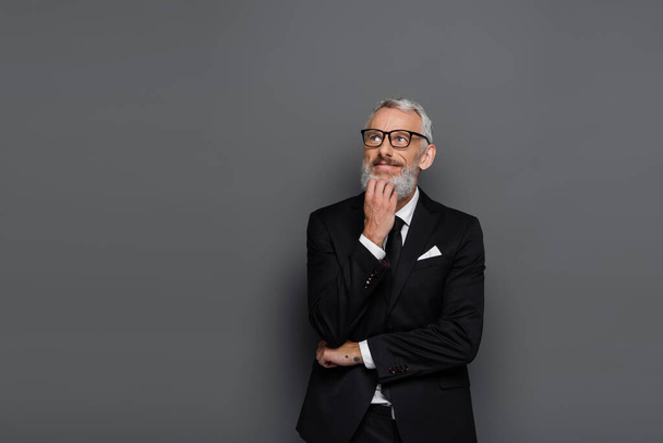 pleased middle aged businessman in suit and glasses thinking on grey - Photo, Image