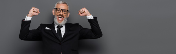 excited middle aged man in suit and glasses rejoicing on grey, banner - Photo, Image