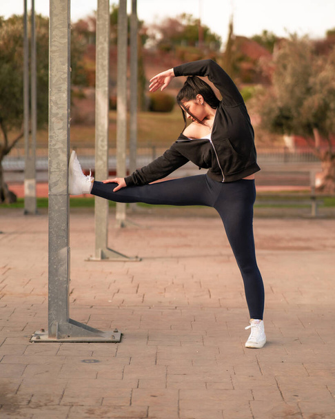 mujer joven y atractiva consultando el mvil en un parque mientras hace yoga y deporte al aire libre - Foto, afbeelding