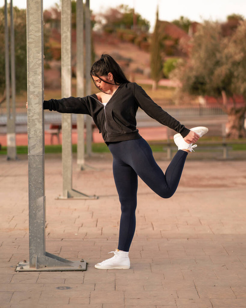mujer joven y atractiva consultando el mvil en un parque mientras hace yoga y deporte al aire libre - Foto, afbeelding