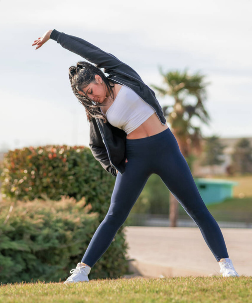 mujer joven y atrativa consultando el mvil en un parque mientras hace yoga y deporte al aire libre - Foto, Imagem