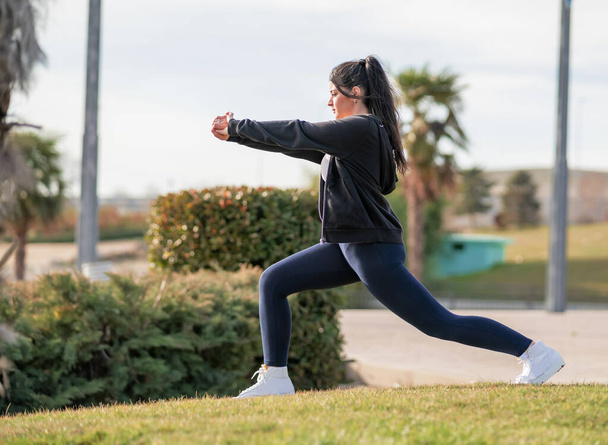 mujer joven y atractiva consultando el mvil en un parque mientras hace yoga y deporte al aire libre - Foto, imagen
