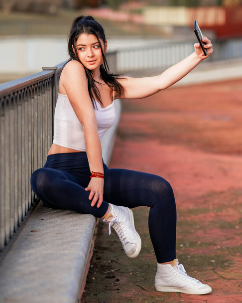 mujer joven y atrativa consultando el mvil en un parque mientras hace yoga y deporte al aire libre - Foto, Imagem