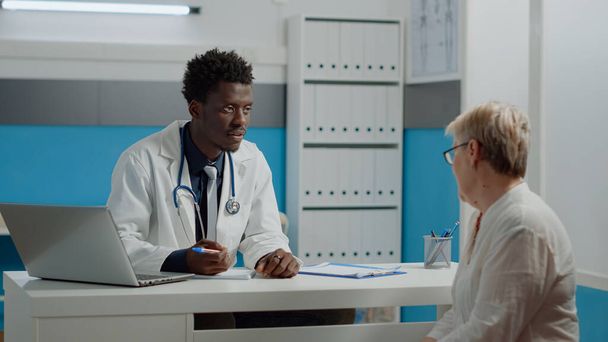 Hombre negro trabajando como médico hablando con una mujer mayor - Foto, Imagen