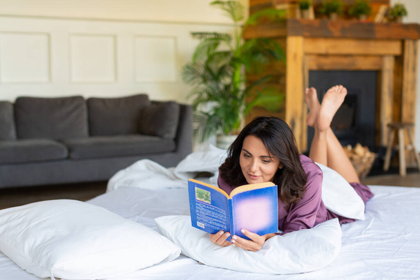 Concept de désintoxication numérique - une femme d'âge moyen se repose allongée au lit en lisant un livre. - Photo, image