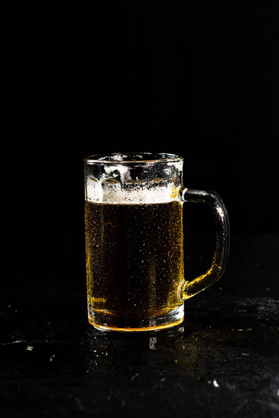 A glass of beer with a foam isolated on a dark background - 写真・画像