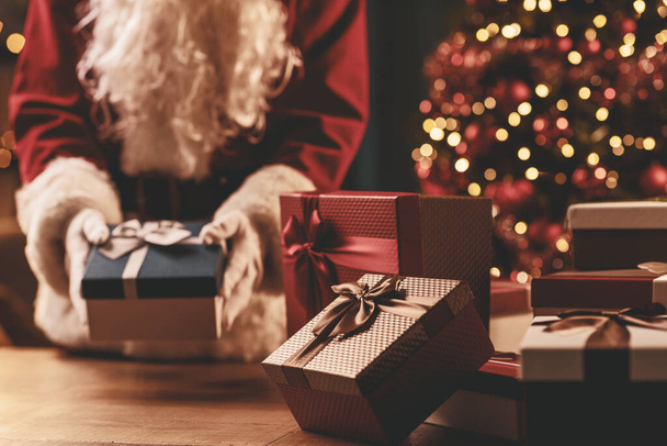 Santa Claus putting Christmas gifts on a table, holiday and celebration concept - Fotoğraf, Görsel