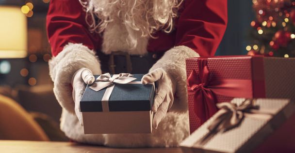 Santa Claus putting Christmas gifts on a table, holiday and celebration concept - Foto, afbeelding