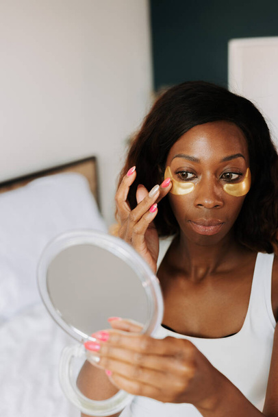 A young beautiful black female applying the anti-fatigue under eye masks - Foto, imagen