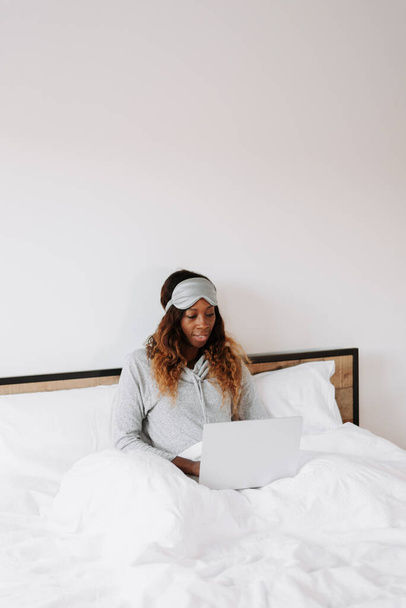 A young beautiful black female on the bed working from home on her laptop - Zdjęcie, obraz