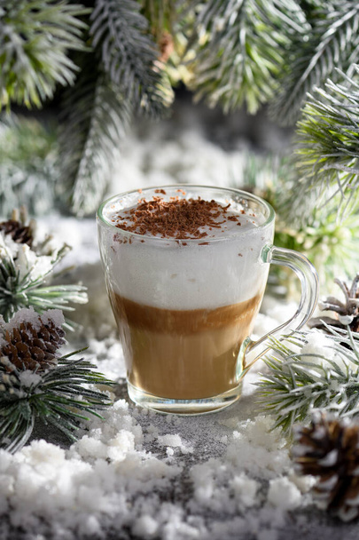 Χριστουγεννιάτικος λάτε μακιάτο. Ένα μεγάλο ζεστό ρόφημα καφέ με ροκανίδια σοκολάτας, ανάμεσα στα χιονισμένα κλαδιά πεύκου και το χιόνι. - Φωτογραφία, εικόνα