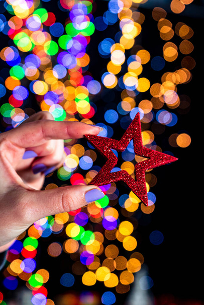 A closeup of a hand holding a Christmas tree star with bokeh lights background - Zdjęcie, obraz