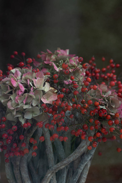 Herbstliches farbenfrohes Arrangement im Korb mit hellvioletten Hortensien und Hagebutten auf dunklem Hintergrund mit Bokeh, hergestellt durch ein Fensterglas - Foto, Bild