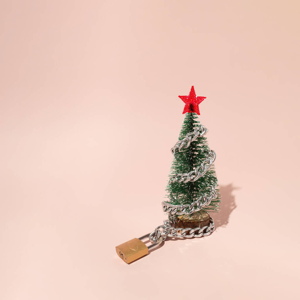 Disposición con un árbol de Navidad con cadena y candado sobre fondo rosa. Estrella roja arriba. El humor de Año Nuevo en el tiempo covid. - Foto, Imagen