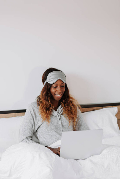 A cheerful young beautiful black female on the bed working from home on her laptop - Foto, immagini