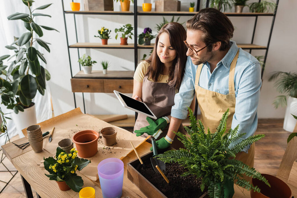 Bloemist houdt digitale tablet in de buurt van collega en planten op tafel in de bloemenwinkel  - Foto, afbeelding