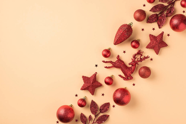 Foto von oben von Reihe Zusammensetzung roten Weihnachtsbaumschmuck Kugeln Sterne Kegel Hirschzweige und Konfetti auf isolierten beige Hintergrund mit Kopierraum - Foto, Bild