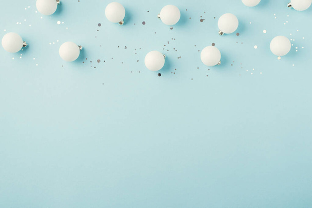 Bovenaanzicht foto van witte kerstboom decoraties kleine ballen en zilver confetti op geïsoleerde pastel blauwe achtergrond met lege ruimte - Foto, afbeelding