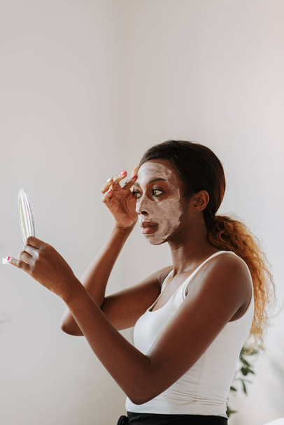 A vertical shot of a black female rubbing the white mask on her face - Foto, afbeelding
