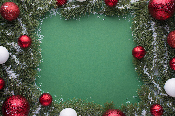 Foto vista superior de bolas de árbol de navidad rojo y blanco sobre ramas de pino nevado sobre fondo verde aislado con espacio en blanco en el centro - Foto, imagen