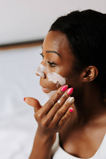 A young beautiful black female applying the mask on her face - Foto, afbeelding