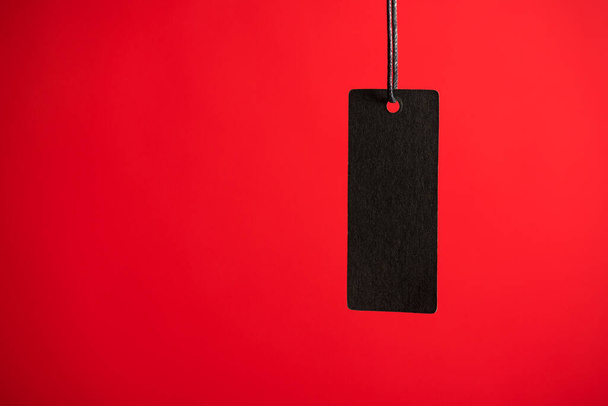 Photo of hanging black price tag on isolated red background with blank space - Foto, afbeelding