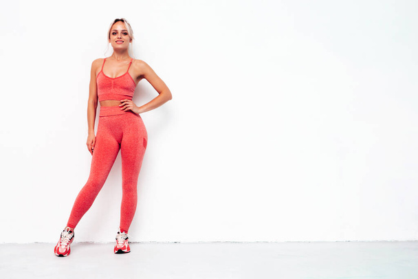 Fitness smiling woman in pink sports clothing. Young beautiful model with perfect body.Female posing near white wall in studio.Cheerful and happy. Stretching out before training - Φωτογραφία, εικόνα