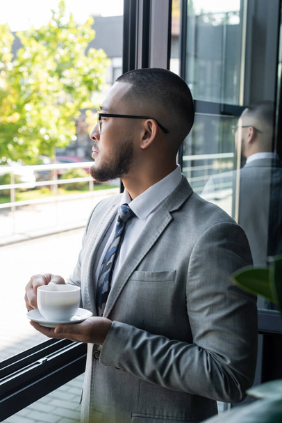 asian businessman with cup of coffee standing near window in office - Fotoğraf, Görsel