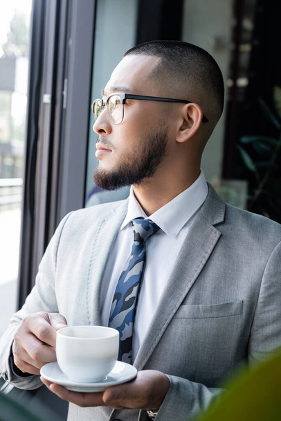 asian businessman in formal wear and eyeglasses holding coffee cup in office - Foto, Imagem