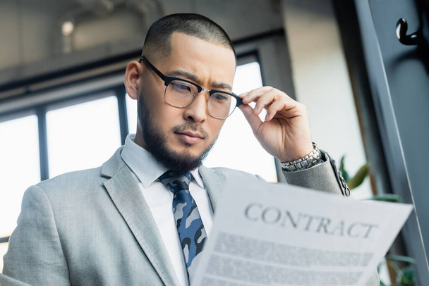 низкий угол зрения азиатского бизнесмена в очках чтение размытый контракт в офисе - Фото, изображение