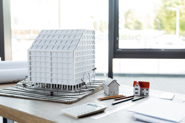 house models, pencils and blurred calculator on desk in construction bureau - 写真・画像