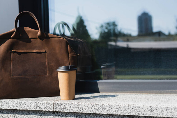 taza de papel con café para ir cerca maletín de cuero marrón en la frontera al aire libre - Foto, Imagen