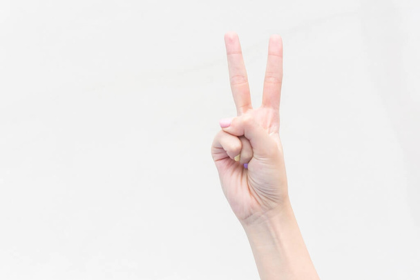 Ruka mladé ženy ukazuje dva prsty jako bojový symbol na izolovaném bílém pozadí. - Fotografie, Obrázek