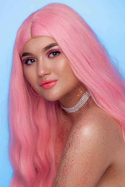 Plus size fashion model, beauty woman with professional makeup glitter on the body and pink hairstyle on blue background, close seup studio shot - Фото, изображение