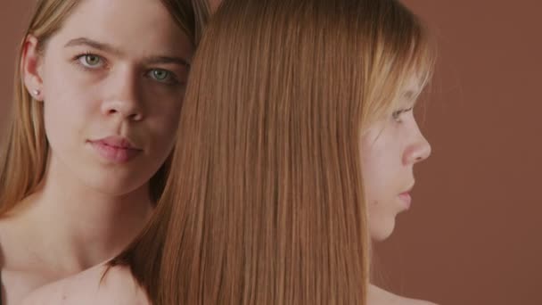 PAN ritratto ravvicinato di giovani donne gemelle in posa per la fotocamera sullo sfondo marrone - Filmati, video