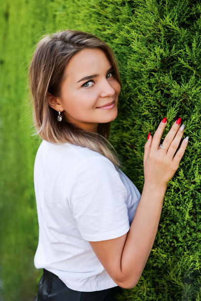 Young woman in white shirt with natural makeup standing by green hedge - Photo, image