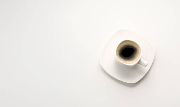 白いテーブルの上のソーサーと白いセラミックカップの黒エスプレッソコーヒー、トップビュー、コピースペース - 写真・画像