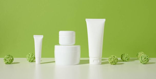 tarro, tubos vacíos de plástico blanco para cosméticos sobre una mesa blanca, fondo verde. Embalaje para crema, gel, suero, publicidad y promoción de productos. Prepárate. - Foto, Imagen