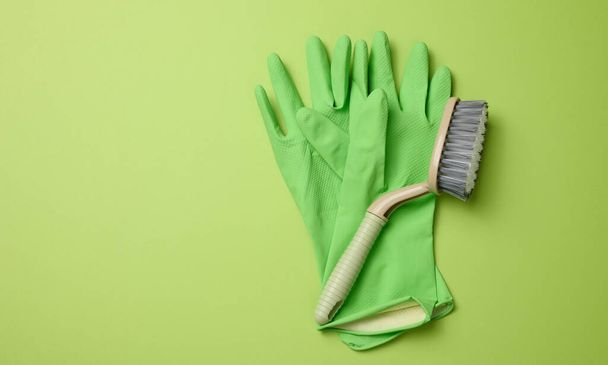 green rubber gloves for cleaning, brushes on a green background, flat lay. Copy space - 写真・画像