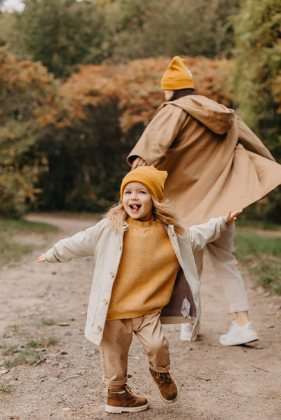 Young happy and smiling mom with her little daughter in arms hugging and kissing spending a weekend on a walk in autumn park. selective focus, noise effect, Autumnal mood - Foto, imagen