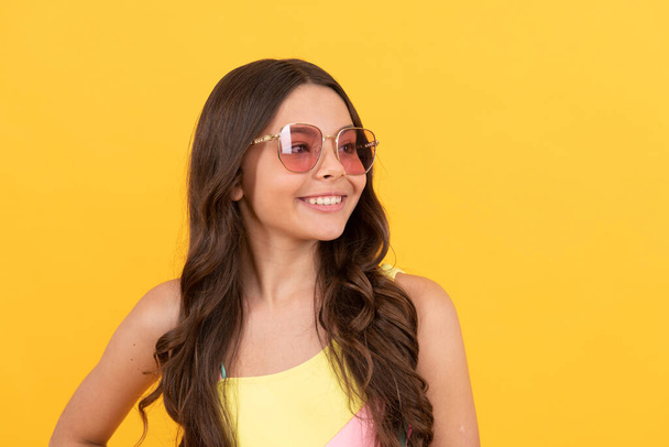 счастливая девочка-подросток в летних очках имеет вьющиеся волосы на желтом фоне, летний портрет - Фото, изображение