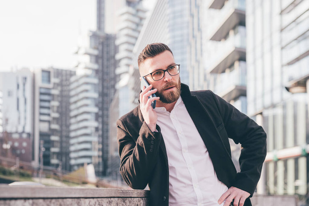 Молодий бородатий кавказький успішний бізнесмен, розмовляючи смартфон, стурбований вирішенням проблеми догляду за клієнтами
 - Фото, зображення