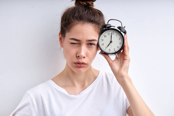 caucasian woman with alarm clock awakening hard early in casual white t-shirt isolated - Fotó, kép