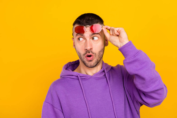 Photo of impressed millennial brunet guy look empty space wear eyewear purple hoodie isolated on yellow color background - Foto, afbeelding