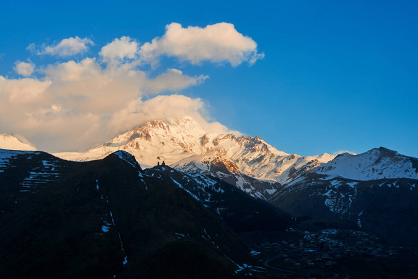 Úsvit v horách. Sluneční paprsky dopadají na vrchol hory Kazbek. Inspirativní ráno pro cestovatele. - Fotografie, Obrázek