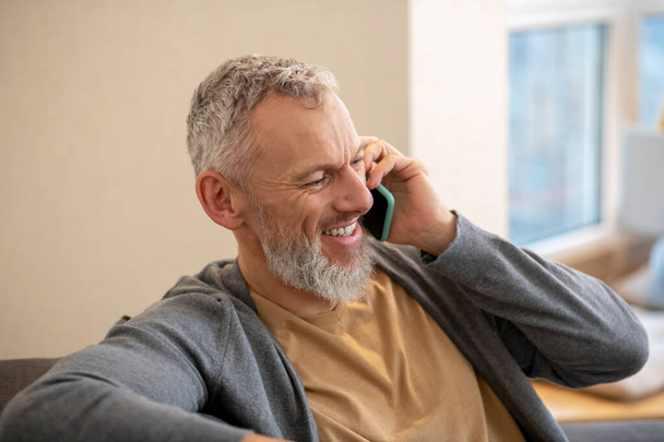 Gri saçlı, olgun bir adam telefonda konuşuyor ve memnun görünüyor. - Fotoğraf, Görsel