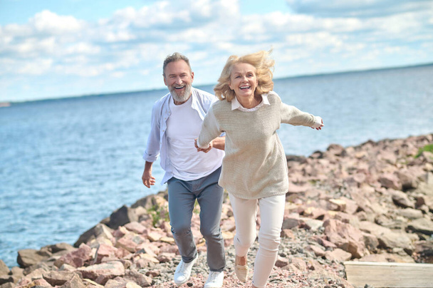 Enthusiastic woman holding mans hand running outdoors - Photo, Image